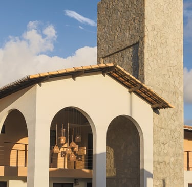 Modern villa with white arches, stone tower, and hanging wicker lanterns against a blue sky.