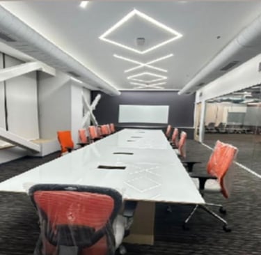 Modern conference room with a long white table, orange ergonomic chairs, and geometric LED ceiling lights.