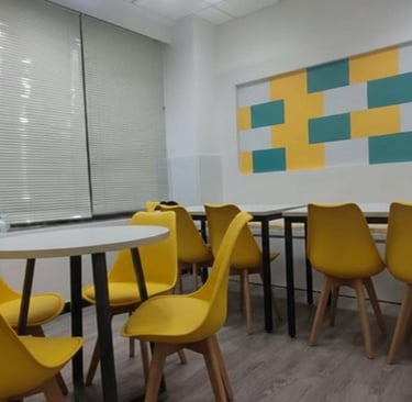 Modern office breakroom with vibrant yellow chairs, round tables, and a coffee machine.