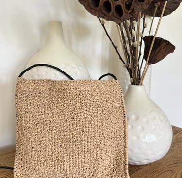 Handknit bag on a wooden table with cream ceramic pots and dried arrangement.