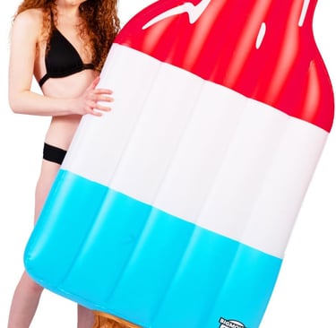 A woman in a black bikini poses with a giant red, white, and blue popsicle inflatable pool float.