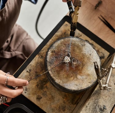 Jewelry maker using a soldering torch on a silver ring at a professional workbench.