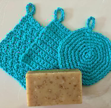 3 crocheted aqua face scrubbies with a bar of soap on top of them