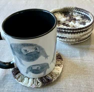 A mug on top of a crocheted drink coaster with more coasters inside a crocheted holder.