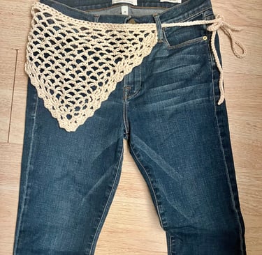 Pair of jeans laid out with crochet bandana belt wrapped around waist