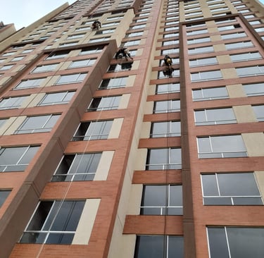 Professional window cleaners rappelling down a modern high-rise brick apartment building to wash exterior glass.