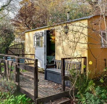 A cozy yellow shepherd's hut with a wooden deck and 'LOVE' sign nestled in a garden.