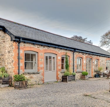 A rustic converted stone barn featuring grey wooden doors and window frames with a gravel patio.