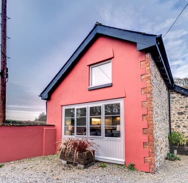 A charming pink cottage with stone walls and large windows, perfect for a cozy vacation rental.
