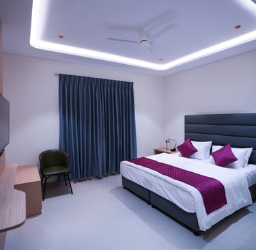 Modern hotel bedroom with purple accents, king bed, and stylish cove ceiling lighting.