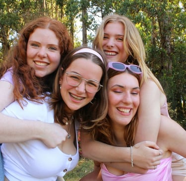 Four smiling women posing for a group photo in a sunny forest setting.