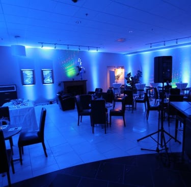 Modern event lounge with blue professional uplighting, cocktail tables, and black chairs.