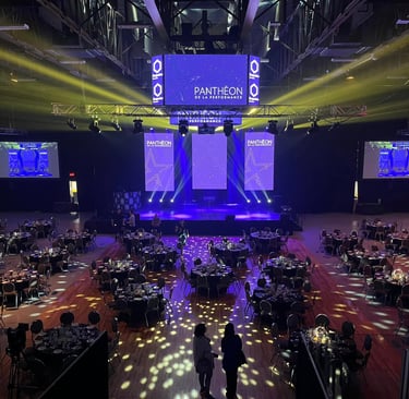 Grand gala ballroom setup with round tables, stage lighting, and large screens for a corporate event.