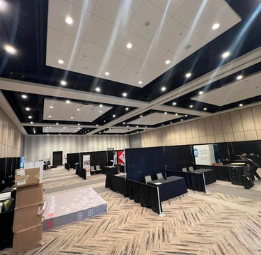 A spacious exhibition hall setup with black draped booths and signage for a corporate trade show event.