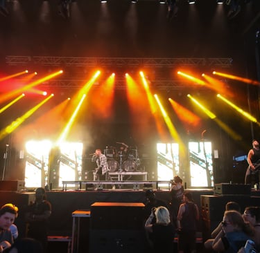 A rock band performs on a large outdoor stage with dramatic orange spotlights and stage lighting.
