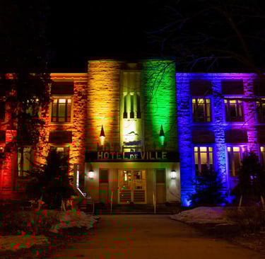 The Hotel de Ville building illuminated with vibrant rainbow pride colors at night.