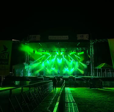 Live music stage at night with bright green spotlights and Rek la Cauze festival banners.