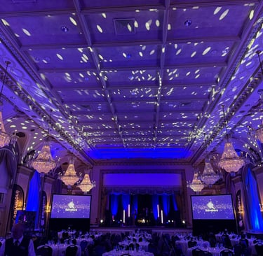 Elegant grand ballroom event space with crystal chandeliers and blue stage lighting for a corporate gala.