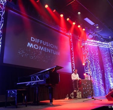 A grand piano on a stage with red and blue concert lighting and a Diffusion Momentum screen.