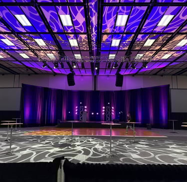 Grand ballroom event space with purple stage lighting, professional audiovisual setup, and high-top tables.