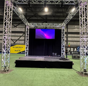 Professional portable event stage with silver aluminum truss system and LED screen on turf.
