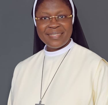Portrait of a smiling Catholic nun wearing a cream habit, black veil, and silver crucifix necklace.