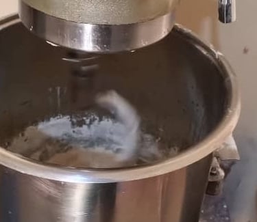 Professional stainless steel stand mixer kneading dough in a large bowl for baking bread.