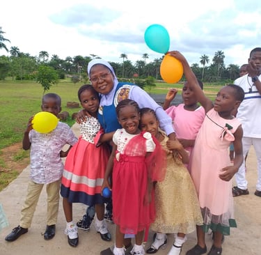 Smiling group of young children and a nun holding colorful balloons at an outdoor charity event.
