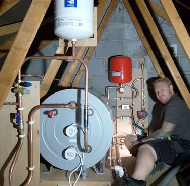 Professional plumber installing a thermal store water tank and expansion vessel in a home attic.