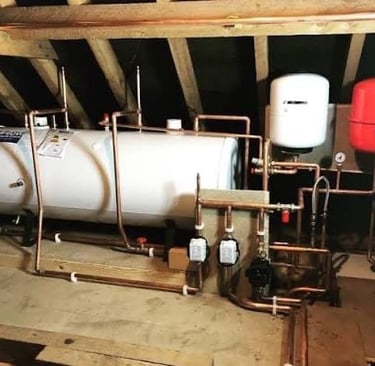 Unvented hot water cylinder with copper piping and expansion vessels installed in a residential loft space.