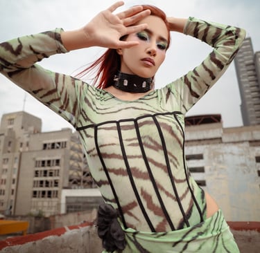 A stylish woman in a green tiger print bodysuit and spiked choker posing on an urban rooftop.