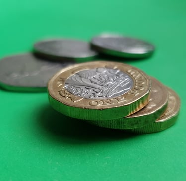 A close-up shot of British one pound coins stacked on a bright green surface.