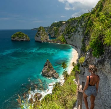 A woman stands on a cliffside path overlooking Diamond Beach and turquoise waters in Nusa Penida, Bali.