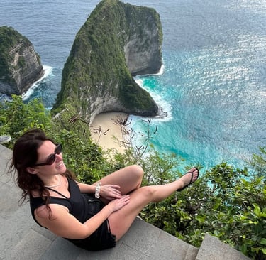 A woman sits on a cliff overlooking the iconic Kelingking Beach and T-Rex Bay in Nusa Penida, Bali.