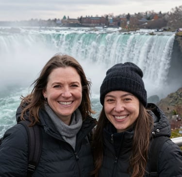 Wide shot of both women standing near the edge of Niagara Falls, their smiles reflecting the sunlight.