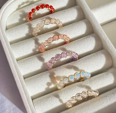 Anillos de cristal envueltos en alambre con cuentas de colores en una caja organizadora blanca.