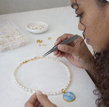 Joyero que utiliza pinzas para armar un collar de perlas blancas con un colgante de Larimar.
