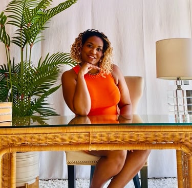 Smiling woman entrepreneur in an orange dress sitting at a glass desk in a bright home office.