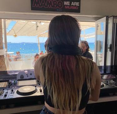 Kat Bendis performing at Cafe Mambo Ibiza booth overlooking the Mediterranean Sea and beach.