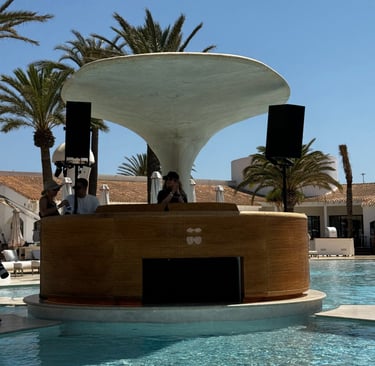 A DJ booth with a mushroom-shaped roof at a luxury pool club with palm trees.