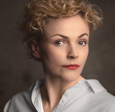 Professional studio headshot of a Maxine Peakewith short blonde curly hair and red lipstick.