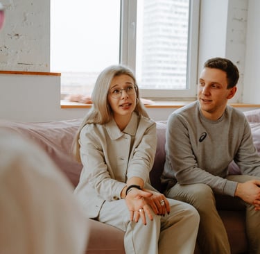 A young couple sitting on a pink sofa in a therapy session discussing relationship issues with a counselor.