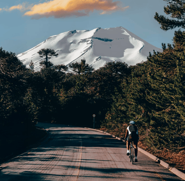 Ciclista recorriendo ruta escénica pavimentada en Lonquimay con vista al Volcán nevado y bosques de 