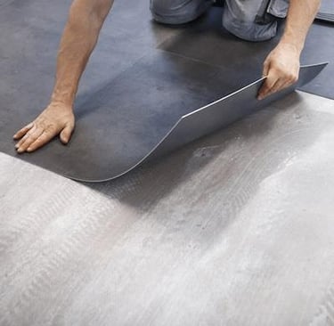 Professional flooring installer laying dark gray vinyl floor tiles over a gray concrete subfloor.