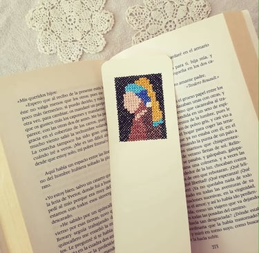 Marcapáginas de punto de cruz con la imagen de La joven de la perla sobre un libro abierto