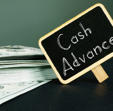 Chalkboard sign with words Cash Advance next to stack of bills