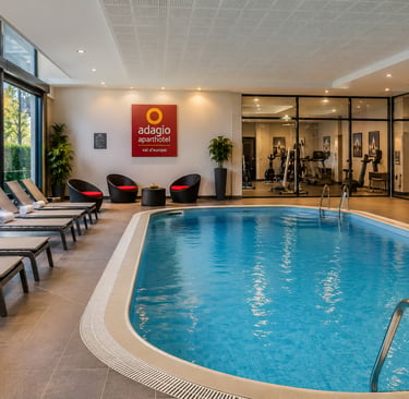 Indoor swimming pool with lounge chairs and fitness center at Adagio Aparthotel Val d'Europe.