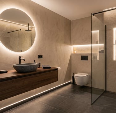 Baño de microcemento: espejo redondo retroiluminado y luz lineal bajo mueble.