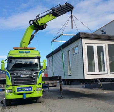 House being lifted onto a truck by a knuckle boom lorry mounted crane.