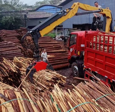 A knuckle boom truck crane loading a large pile of wood onto a truck.